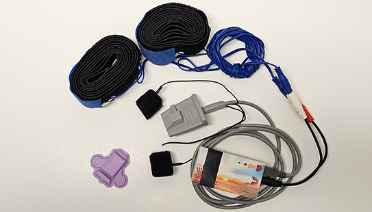 The wearable polygraph device (purple) is shown next to a standard polygraph system.
